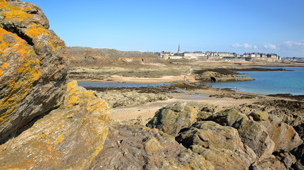 View of the walled city of Saint Malo from Petit Be Island at low tide, Saint Malo, Brittany, France, with colorful rocks in the foreground