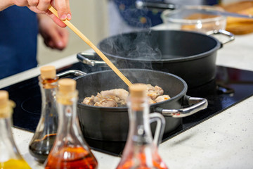 Man cooks meat in a frying pan. Hand using spatula to stir red and white frying pan full of meat
