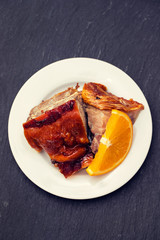 roasted piglet with orange on white plate on black background