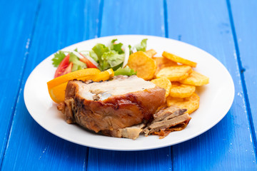 roasted piglet with potato chips and orange on white plate