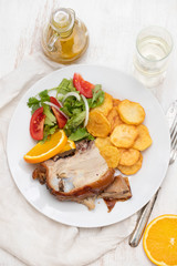 roasted piglet with potato chips and orange on white plate