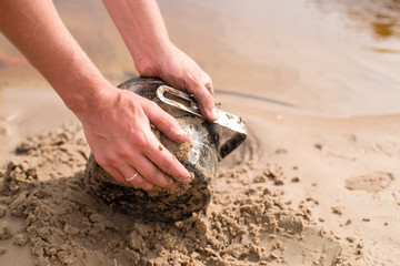Female hands polish in sand at the river burned on a fire an aluminum kettle. Washing of ware on vacation, in a campaign