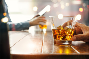 Close-up of two men clinking whiskey drink alcoholic beverage at bar counter in the pub background.