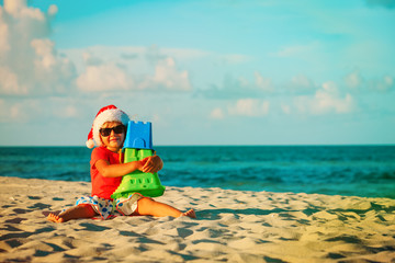 happy little girl play with sand and toys on beach at christmas