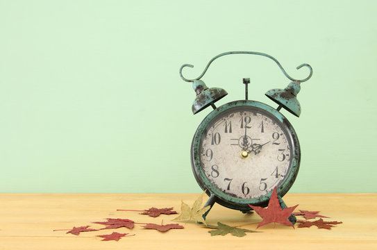 Image of autumn Time Change. Fall back concept. Dry leaves and vintage alarm Clock on rustic wooden table.