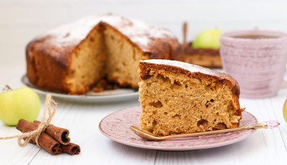 Pie with apples, cinnamon and ginger on a white background. A piece of cake in the foreground. On the photo, apples, cinnamon sticks and a cup of coffee.