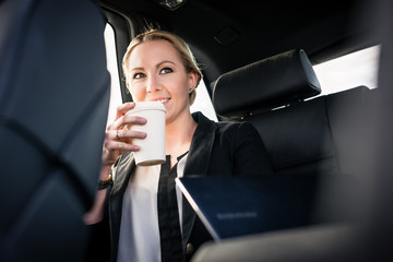 Smiling young businesswoman drinking takeaway coffee in car