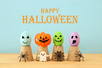 Halloween holiday concept. Colorful eggs with funny, scary and cute faces, spiders over wooden...