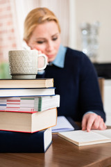 Stack of books with mug on top in front of woman reading book