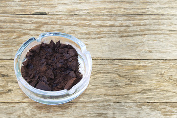 Glass Ashtray Filled with Used Coffee Ground on Wooden Table