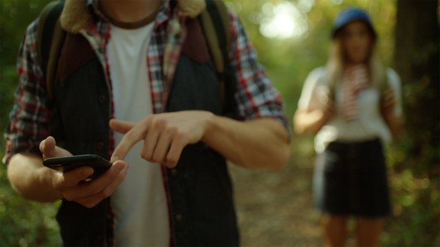 Young man with phone in his hands navigating group of backpackers on hiking in the forest