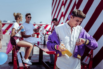 It is time. Handsome brunette male holding bottles of beer while checking time on watches