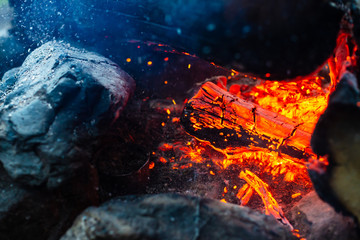 Smoldered logs burned in vivid fire close up. Atmospheric background with orange flame of campfire. Unimaginable detailed image of bonfire from inside with copy space. Smoke and glowing embers in air.