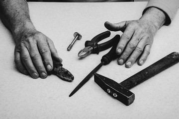 Table composition with tools (nippers, hammer, pliers, rasp, bolt) and hands of elderly working man...