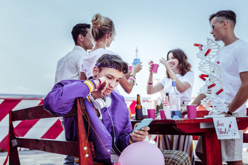 Cocktail party. Attentive boy leaning on bench while looking at telephone