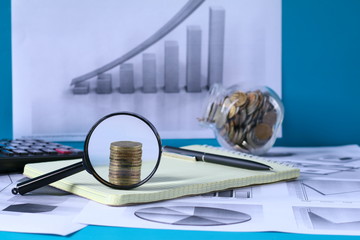 The concept of business, finance and investment. Notebook, graphics, magnifying glass, calculator, pen, notepad, coins on blue wooden background.