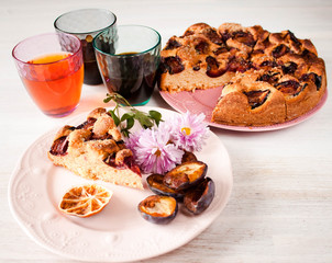 Homemade sweet round plum cake New York Times and cut n saucer with cups, glasses of tea, coffee on family holyday Breakfast or birthday party on white table. Side veiw. Selective focus.