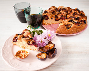 Homemade sweet round plum cake New York Times and cut n saucer with cups, glasses of tea, coffee on family holyday Breakfast or birthday party on white table. Side veiw. Selective focus.
