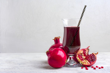 Red pomegranate juice in a glass, ripe and cut pomegranate and a sprig of mint on a gray concrete...