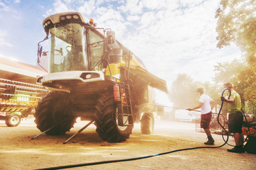 The mechanics repair the yellow combine harvester in the farm yard.