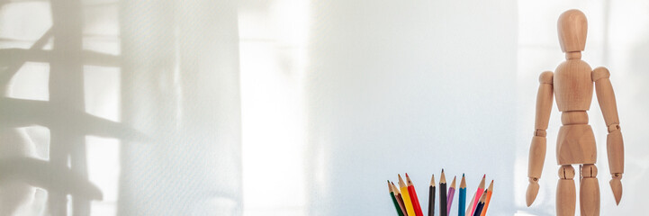Panoramic photo with pencils and a wooden puppet on the background of a window with a curtain
