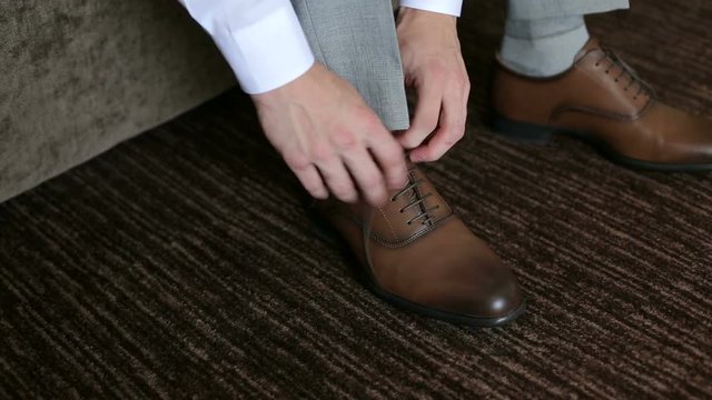Man ties up shoelaces on brown leather shoes, close-up.