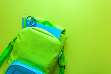 Back to school concept. Green backpack with school supplies on green background. Top view. Copy space