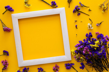 Colorful bouquet of dried autumn flowers and white wooden frame lying on yellow paper background. Copy space. Flat lay. Top view. Greeting card. Flowers composition.
