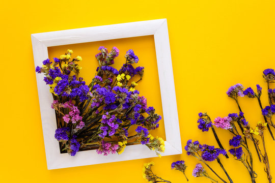 Colorful bouquet of dried autumn flowers lying on a white frame on yellow paper background. Copy space. Flat lay. Top view. Greeting card. Flowers composition.