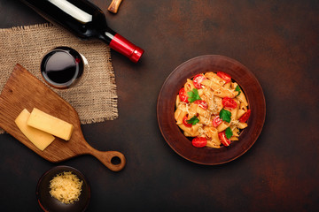 Pasta with cheese, cherry tomato sauce, wineglass and bottle wine on rusty background