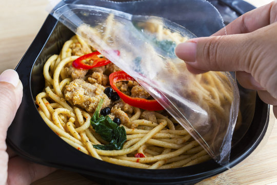 Take-away food ready meal: Woman hands holding open cling wrap and take out food in plastic boxes on wood background. Concept online order food delivery service for home delivery.