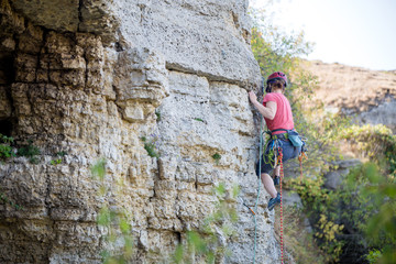Fototapeta premium Photo of side view of young athlete woman in red helmet climbing up mountain