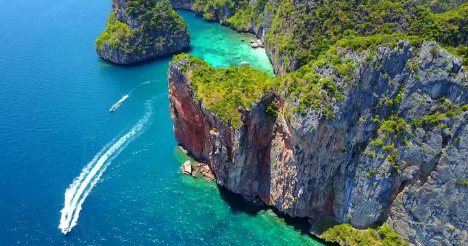 Aerial Overhead Approaching View of Loh Samah Bay, Thailand With Large Boat Moving Past Rocky Cliff Coast