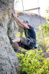 Photo of athlete man in helmet clambering over rock against background of green trees