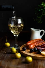 Foto op Plexiglas Aperitif concept. Wine pours into a glass goblet. On the table, meat appetizer, fried sausages, salami, cheese, olives. © Natalya