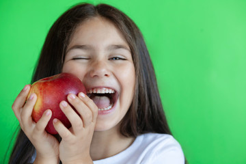 Happy child girl eat apple isolated on green background. Kid with fruits.