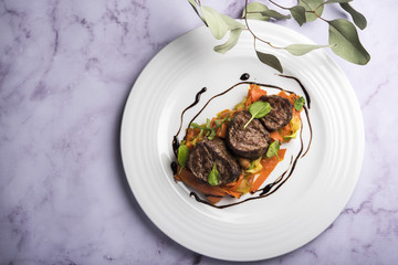 Meat medallions with sauce and carrot on a white plate