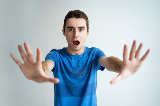 Worried attractive man showing stop gesture with palms. Young guy frowning, screaming and looking at camera. Stop gesture concept. Isolated front view on white background.
