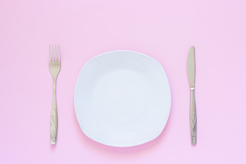 White plate and fork, table-knife on pink background