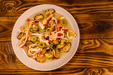 Ceramic plate with different sea food and olives on wooden table. Top view