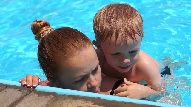 A young mother teaches her little son to swim in the pool in the summer on vacation. Happy little boy swimming in pool with mom. Slow motion. Close-up.