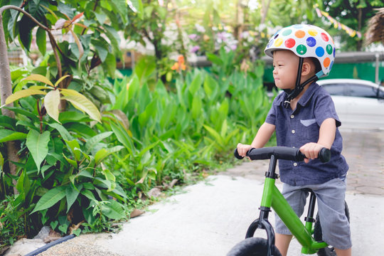 Cute little Asian 2 years / 30 months old baby boy child wearing safety helmet learning to ride first balance bike in sunny summer day, kid playing & cycling at park, Cycling with young kids concept