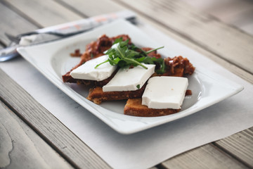 Poach fried toasted bread slices poach fried with pancetta, fresh cow cheese and rocket leaves served in plate. Selective focus