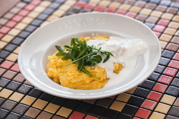 Fresh made cooked polenta served with cream cheese sauce and rocket leaves - rucola in plate at dining table