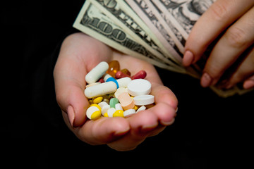 Money and pills in hands, isolated on black. Wasting too much money on medication. Drug addiction concept