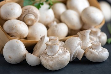 Set of fresh whole and sliced champignon mushrooms in a basket on a dark background. Close Up