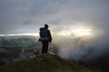 Hiker Watching the Sunset through the Clouds over the Landscape