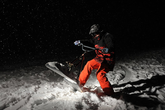 Snowboarder in orange sportswear jumping on a snowy hill at night