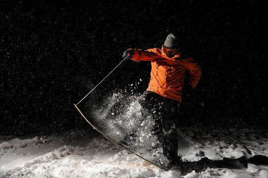 Snowboarder in orange sportswear and mask jumping on a snowy hill at night