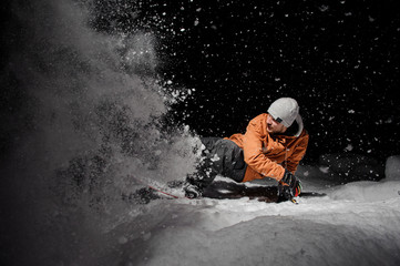Snowboarder in orange jacket riding on a snowy hill at night